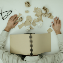 Exhausted man with head on desk surrounded by scattered stationery, illustrating ad fatigue.