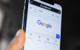A close-up of a person's hand holding a smartphone showing the Google search homepage.